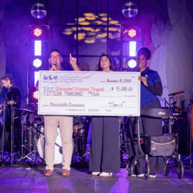 $ALT TEXT: People on stage holding a large charity donation check during a Disney-themed event.