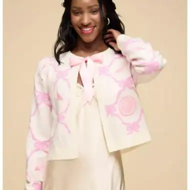 Disney fashionista wearing a stylish pink and cream cardigan with bows and a satin dress, showcasing Disney-inspired fashion trends.