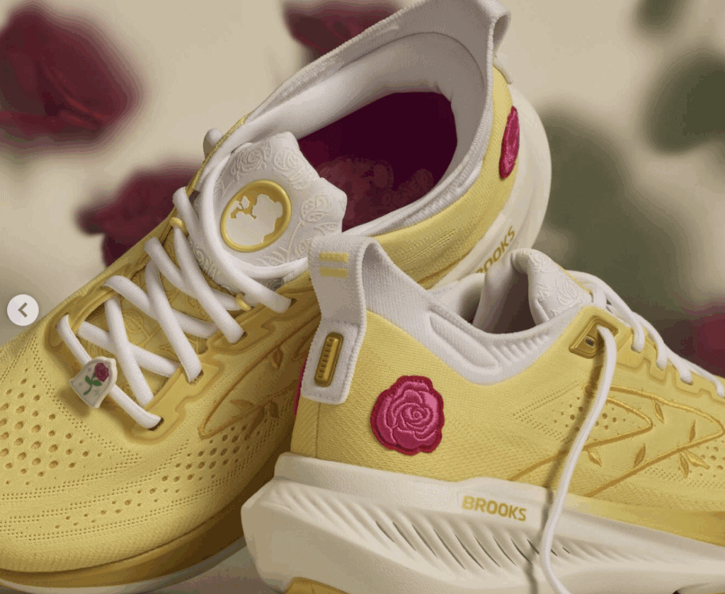 Yellow Disney-themed Brooks sneakers with pink rose accents and white laces.