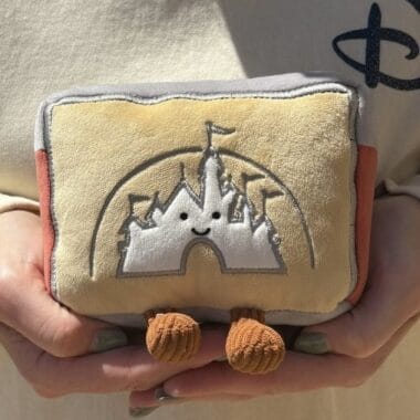 Cute plush toy of Disney castle with smiling face and orange feet.