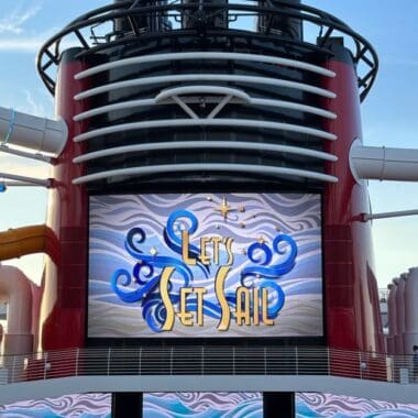 Large outdoor screen on Disney cruise ship with 'Let's Get Sail' graphic.